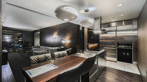 Moderni hotellihuone, jossa on ruokailutila, ruostumattomasta teräksestä valmistetuilla laitteilla varustettu keittiö ja näkymä kaupunkiin.