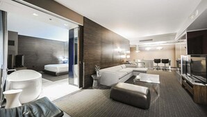 Moderni hotellihuone, jossa on suuri sänky, oleskelualue sohvineen ja rahiineen, pieni keittiö ja televisio.