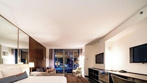 A modern hotel room with a large bed, a desk with a TV, a sofa, and a view of a cityscape. - SVS: Strip View Studio | Open Balcony | Resort Amenities | Palms Place (Las Vegas)