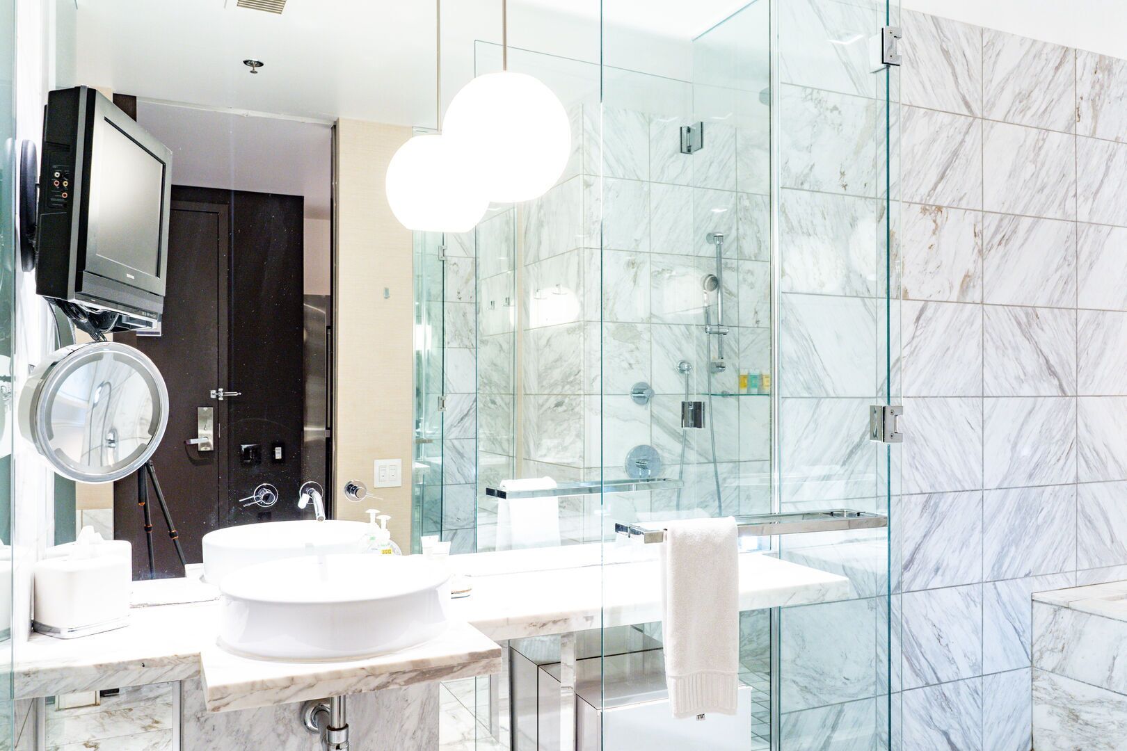 A modern bathroom with a glass shower enclosure, a round mirror, and a white sink.