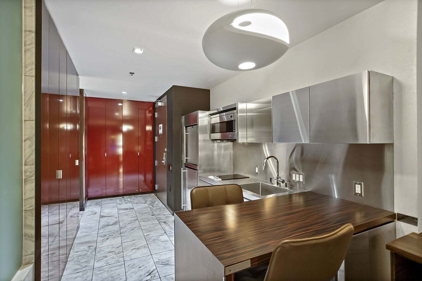 Une cuisine moderne équipée d’appareils électroménagers en acier inoxydable, une table à manger en bois et une porte rouge.