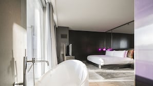 Una camera d'albergo moderna con una vasca da bagno grande, un letto con testiera e una televisione.