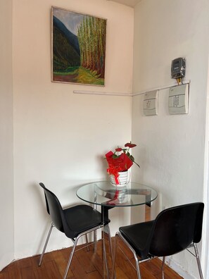 A room with a glass table, two black chairs, a painting of a forest, and a vase with red flowers. - Centrally located apartment 393+wifi+hot water (Cusco)