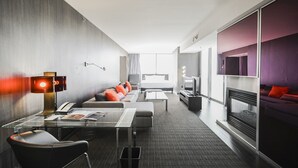 Moderni hotellihuone, jossa on sohva, televisio, takka ja työpöytä lampun kanssa.