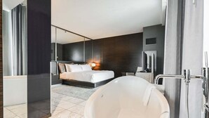 A modern hotel room with a large bathtub, a separate shower area, a bed with a headboard, and a large mirror. - SVS: 1BD Strip View | Jetted Tub | Full Kitchen | Sleeps 6 | Palms Place (Las Vegas)