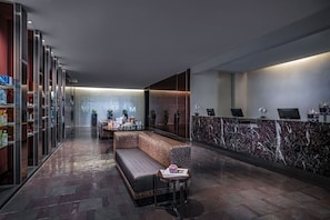 Un área de recepción moderna con una barra de mármol, una zona de estar con un banco y una pequeña mesa, y una pared de vidrio con un diseño decorativo.