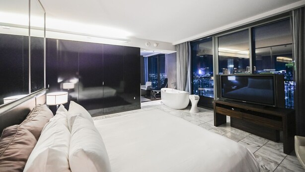A modern hotel room with a large bed, a bathtub, a TV, and a city view. - SVS: High Floor 1BD | Full Kitchen | Jetted Tub | Sleeps 4 | Palms Place (Las Vegas)