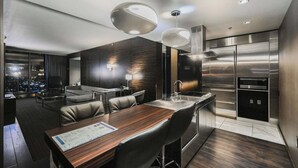 Ein modernes Hotelzimmer mit Essbereich, einer Küche mit Edelstahlgeräten und Blick auf die Stadt.