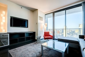 A modern living room with a large TV, a red chair, a glass coffee table, and a city view through large windows. - SVS: Strip View Studio | Open Balcony | Pool & Gym | Palms Place (Las Vegas)