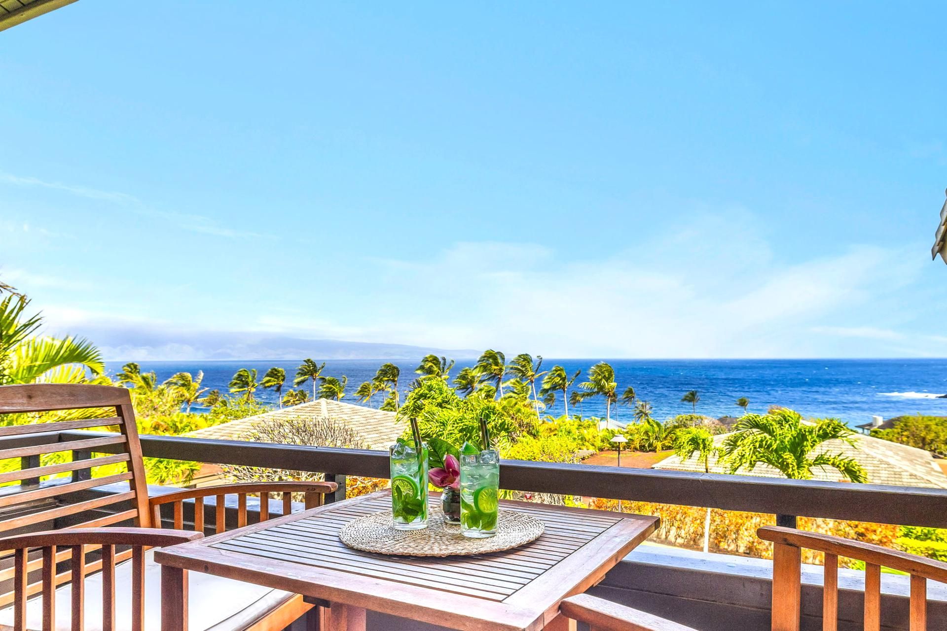 Une terrasse en bois avec une table et des chaises, donnant sur une plage bordée de palmiers et sur l’océan.