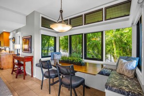 A modern kitchen with a dining area, large windows with tropical views, and a seating area with a view. - Kapalua Ridge Villas | Ocean View 1 BR, Sleeps 4 | Car Incl. w/ 6+ Nights | KRV-311 by KBM (Lahaina)