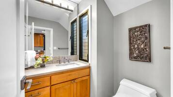 A bathroom with a white toilet, wooden cabinets, a large mirror, and a wall-mounted artwork.
