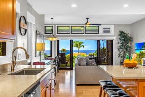 A modern kitchen with a view of the ocean, a dining area with a view, and a living area with a sofa and a coffee table.
