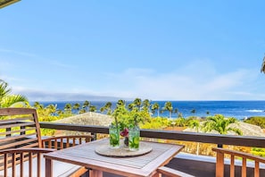 A wooden table with two glasses of a green beverage, a woven placemat, and a view of the ocean with palm trees. - Kapalua Ridge Villas | Ocean View 1 BR, Sleeps 4 | Car Incl. w/ 6+ Nights | KRV-311 by KBM (Lahaina)