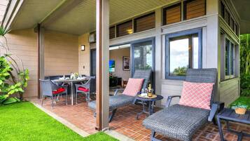 A covered patio with wicker furniture, a dining table, and a small table with a bottle.