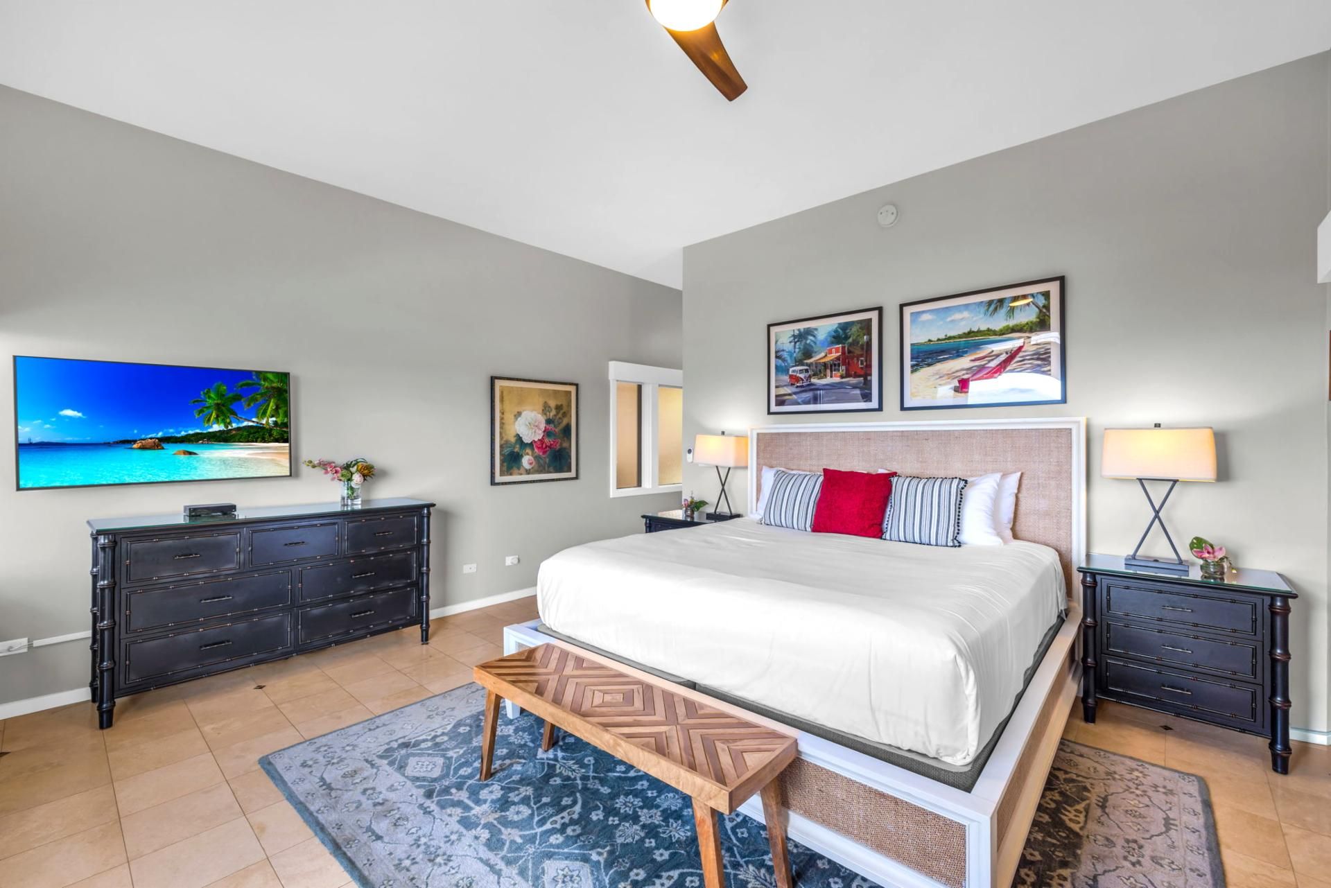Une chambre à coucher comprenant un lit, une commode, des tables de chevet, un téléviseur et des œuvres d’art accrochées aux murs.