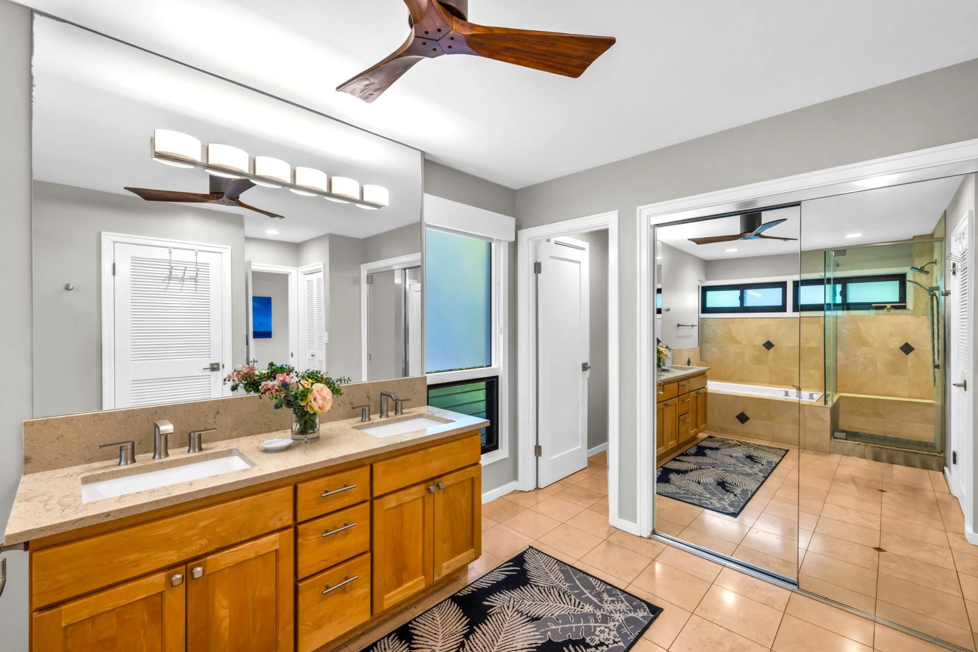 A modern bathroom with a dual sink vanity, a ceiling fan, and a glass shower enclosure.