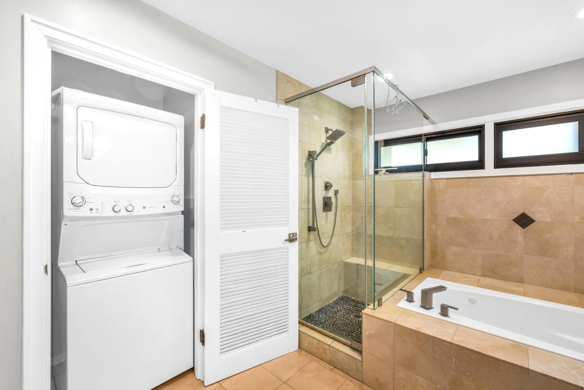 A modern bathroom with a glass-enclosed shower, a built-in washer-dryer unit, and a separate bathtub.