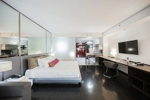 Quarto de hotel moderno com uma cama grande, uma escrivaninha, uma televisão e um espaço de refeições separado.