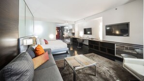 Una habitación de hotel moderna con cama, sofá, televisión y kitchenette.
