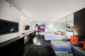 Ein modernes Hotelzimmer mit großem Flachbildfernseher, einer Couch, einem Bett, einem Schreibtisch und einem Spiegel.