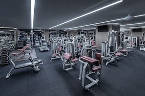 Ein modernes Fitnessstudio mit verschiedenen Trainingsgeräten, Spiegeln und einem Deckenventilator.