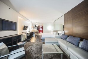 Habitació d'hotel moderna amb televisió de pantalla plana, sofà, taula de cafè, zona de dinar i dormitori separat amb llit i nitzeta.
