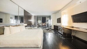 A modern hotel room with a large bed, a desk, a TV, and a view of the city at night. - Palms Place Studio | Strip View & Balcony (Las Vegas)