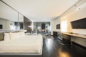 Ein modernes Hotelzimmer mit einem großen Bett, einem Schreibtisch, einem Fernseher und Blick auf die beleuchtete Stadt bei Nacht.