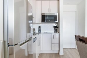 A compact kitchen with white cabinetry, a stainless steel refrigerator, and a microwave. - Landing | Amazing Studio, Gym, Yoga Studio (Golden Gate)