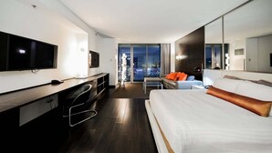 Una habitación de hotel moderna con una cama grande, un escritorio con televisor, un sofá y un balcón con vista a la ciudad.