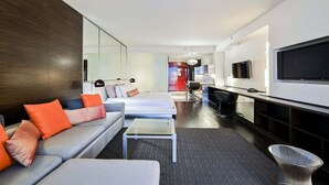 Ein modernes Hotelzimmer mit einer Couch, einem kleinen Tisch, einem Fernseher und einer Küchenzeile.