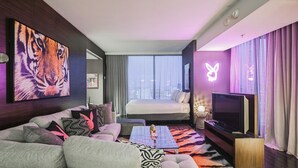 Ein modernes Hotelzimmer mit einem großen Bett, einer Couch, einem Fernseher und Blick auf die Stadt.