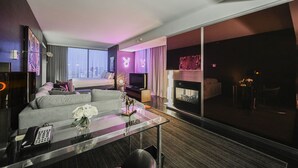 Ein modernes Hotelzimmer mit einem großen Bett, einer Couch, einem Fernseher, einem Kamin und Blick auf die Stadt.
