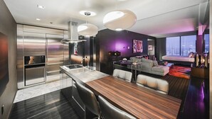 Eine moderne Küche mit Edelstahlgeräten, ein Essbereich mit Holztisch und ein Wohnbereich mit Sofa und Blick auf die Stadt.