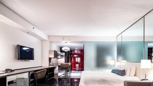 Ein modernes Hotelzimmer mit Flachbildfernseher, Schreibtisch mit Stuhl, einem Bett mit Kissen und einem großen Spiegel.