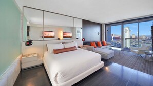 Een moderne hotelkamer met een groot bed, een sofa, een balkon met uitzicht over de stad en een grote spiegel.