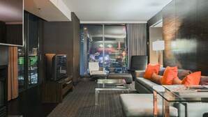 A modern hotel room with a city view, a flat-screen TV, a sofa with orange cushions, and a glass coffee table. - SVS: 1BD Strip View | Jetted Tub | Full Kitchen | Sleeps 4 | Palms Place (Las Vegas)