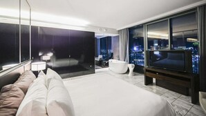 A modern hotel room with a large bed, a seating area, a bathtub, a television, and a city view. - SVS: 1BD Strip View | Jetted Tub | Full Kitchen | Sleeps 4 | Palms Place (Las Vegas)