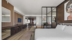 Ett modernt hotellrum med en stor säng, ett skrivbord, en sittgrupp och utsikt över köksdelen.