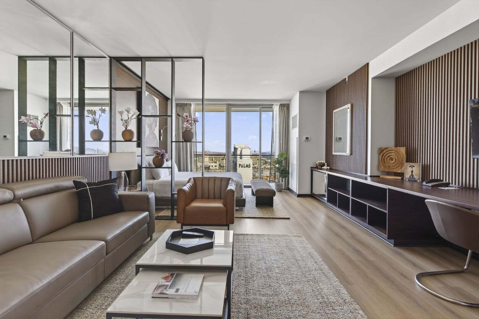 A modern living room with a sofa, armchair, coffee table, and a desk area with a computer.