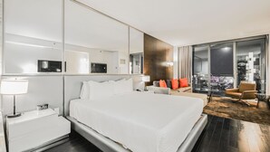 Une chambre d’hôtel moderne dotée d’un grand lit, d’une table de chevet, d’un canapé, d’un fauteuil et d’une grande fenêtre donnant sur la ville.