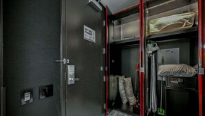 Une chambre compacte et moderne, équipée d’un lit, d’une petite table et d’un meuble de rangement contenant un oreiller et une couverture.
