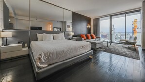 Moderni hotellihuone, jossa on suuri sänky, sohva, sohvapöytä ja parveke, jolta on näkymä kaupunkiin.