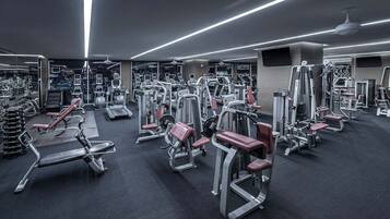 Une salle de sport équipée de divers appareils d’exercice, de miroirs et d’un ventilateur au plafond.