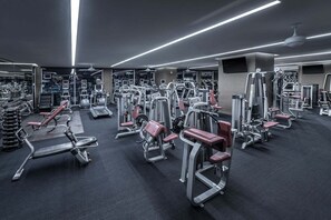 Ein Fitnessstudio mit verschiedenen Trainingsgeräten, Spiegeln und einem Deckenventilator.