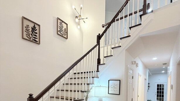 A staircase with white railings and dark wood steps, leading to a landing with a small table and framed artwork. - GHome, Modern Cozy 5BR 10BEDS located  in Lilburn, GA with AC perfect for family (Lilburn)