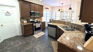 A modern kitchen with dark marble floors, stainless steel appliances, and brown cabinetry. - GHome, Modern Cozy 5BR 10BEDS located  in Lilburn, GA with AC perfect for family (Lilburn)