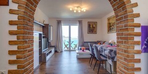 A room with a TV, a dining table with chairs, a balcony with a view, and brick walls. - Holiday flat (Mali Lošinj)