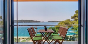 A balcony with a table and chairs, overlooking a body of water and a distant shoreline. - Holiday flat (Mali Lošinj)